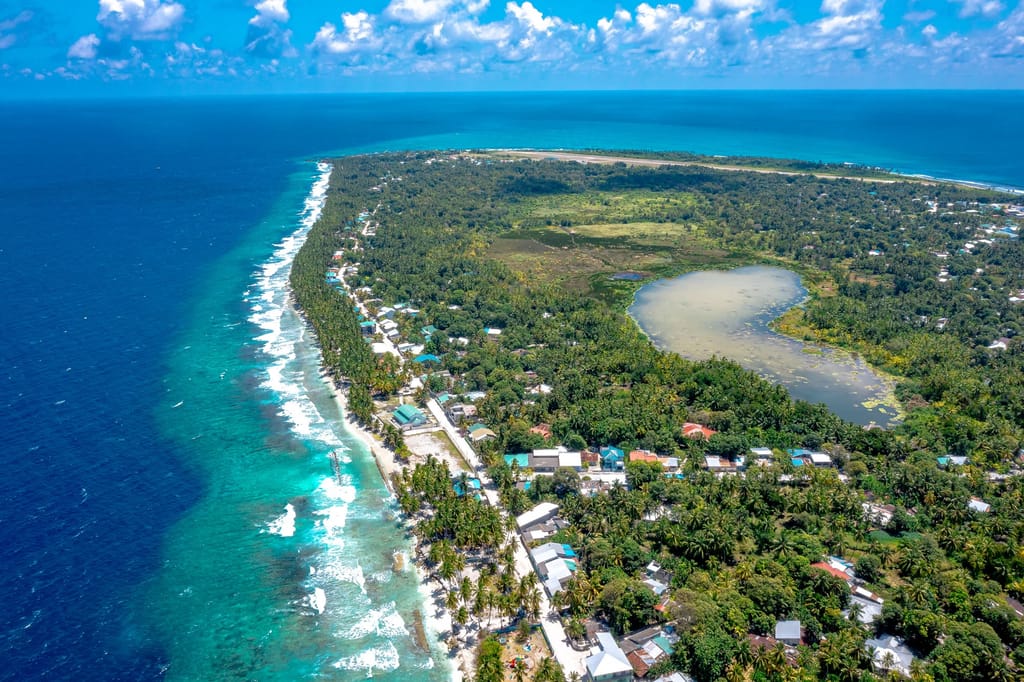 Aerial view of Fuvahmulah’s southern tip with the surf line, reef and town under coconut palms