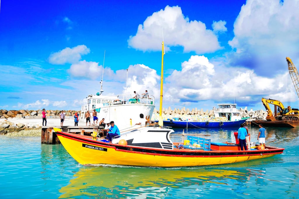 Yellow fishing dhoni moored at Fuvahmulah harbour with fishermen on deck