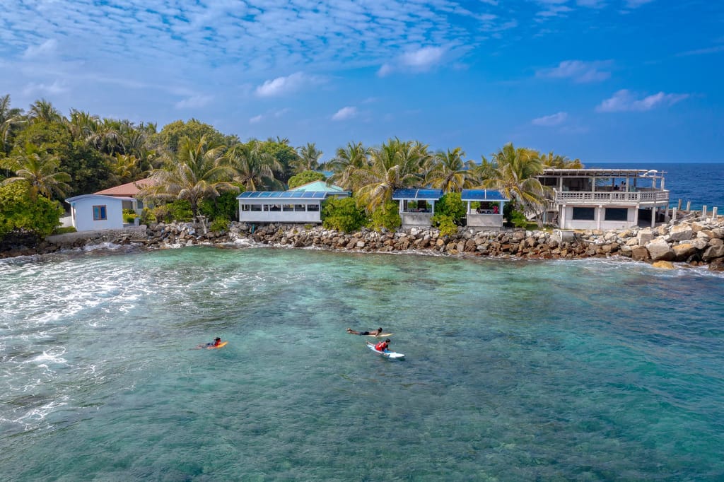 Sheltered turquoise water beside houses and a stone breakwater, with swimmers
